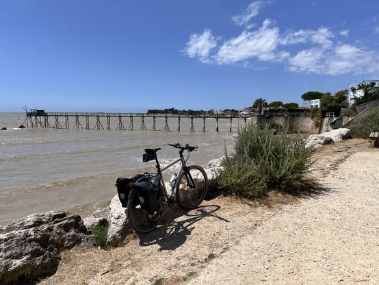 Mon vélo appuyé sur un rocher, devant la mer assez agitée . Au loin un carrelet, petite cabane sur pilots pour pêcher au filet.
