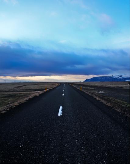 a 2 lane highway stretches out into the distance, seemingly forever, with no one in sight, a beautiful but forlorn blue bank of clouds drifts in from the ocean refracting a world of twilight
