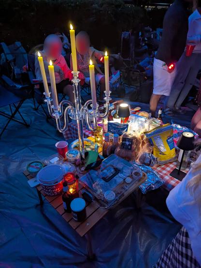 Our picnic table with a spread of food, drinks, and a candelabra as a centerpiece with smaller LED lamps around it.