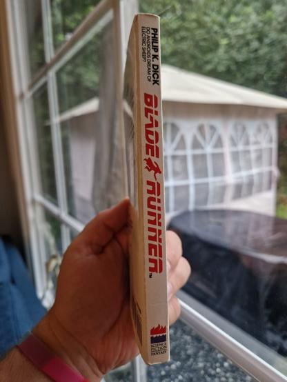 I am holding the same book, this time from an angle that shows the spine, which is smooth and shiny, clearly lacking the wrinkles one would expect on a pocket book that has been read.