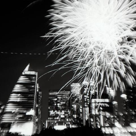 Black and white photograph of fireworks over downtown Austin, TX. The path of a drone is visible as a dotted line through the middle of the image.