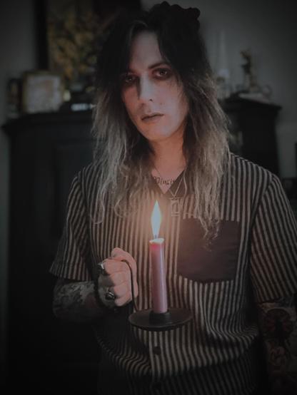 Me standing in a dimly lit and cluttered room with a candle in a cast iron holder illuminating my face