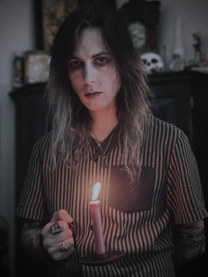 Me standing in a dimly lit and cluttered room with a candle in a cast iron holder illuminating my face