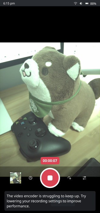 A screenshot of Plasma Camera in its video UI on the OnePlus 6, with the viewfinder showing a plushie dog on an xbox controller. A video is being recorded, showing the current timestamp at 7 seconds. A warning is displayed that the video encoder is struggling to keep up.