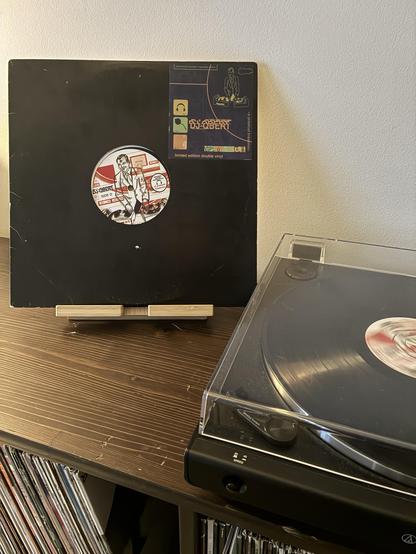 A vinyl record cover of DJ QBert’s Demolition Pumpkin Squeeze Musik (black with a sticker with artwork and the title and artist) next to a turntable playing the record