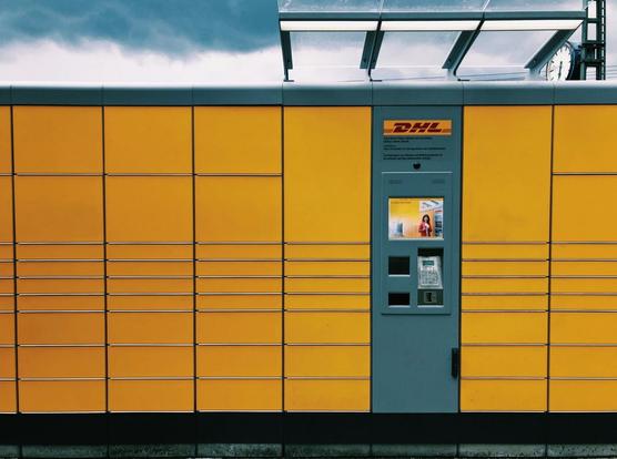 Frontalansicht einer DHL-Packstation, im Hintergrund blauer Himmel mit weißen Wolken.