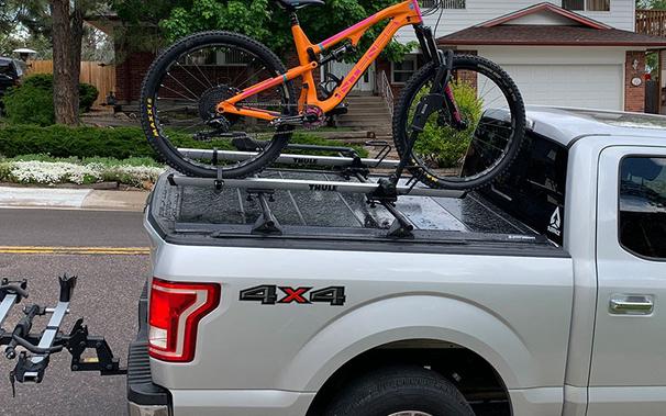 Picture of an F150 short-box pickup with a tonneau cover, with a bike rack mounted on the bed rails of the truck box and an expensive looking bike in the rack. For some reason there’s a second, empty bike rack mounted on the truck’s trailer hitch.