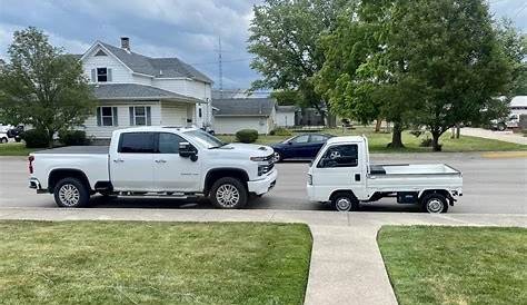 Photo of a white Japanese ‘kei’ truck parked nose-to-nose with typical late-model Chevy pickup. Despite the obvious difference in size (the Chevy dwarfs the kei truck), the cargo bed in the kei appears larger.