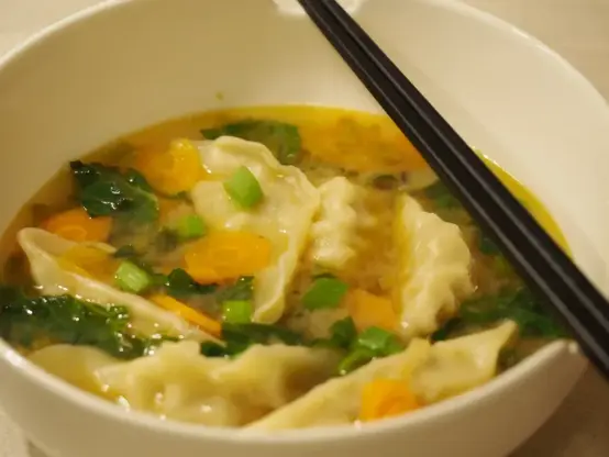 Die fertige Suppe in einer weißen Suppenschüssel an deren Rand zwei schwarze Essstäbchen liegen.