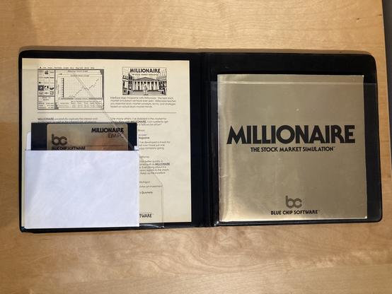 The interior of the Millionaire folio case, showing a faux gold-gilt manual, diskette with gold label, and an ad sheet for the game.