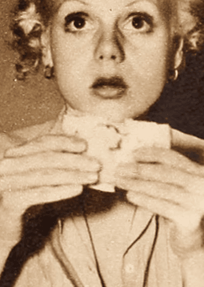 Una joven sosteniendo un sándwich, con una expresión de sorpresa o asombro, en una imagen en blanco y negro.
