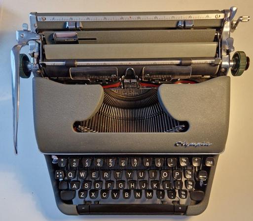 A photo of a typewriter as seen from above. It it matte green, with black plastic keys in standard UK layout
