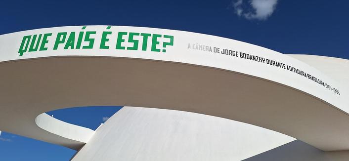 Alça branca do MuN sob o céu azul. Está plotado em sua lateral o título da exposição QUE PAÍS É ESSE? a câmera de Bodanzky durante a ditadura brasileira 1964-1985