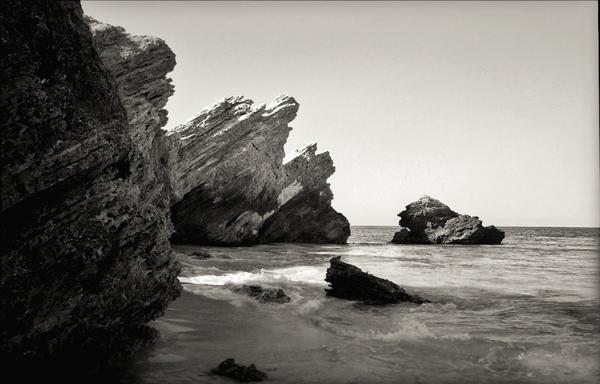 a lunar-esque feel to a high contrast beach scene, with rocky white / gray crags and bright blue water and silvery sky