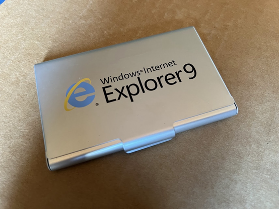 Slim silver aluminum case, approximately the size of a business card holder. On the front is "Windows Internet Explorer 9" and the old Internet Explorer lower-case "e" logo with a yellow orbit around it.