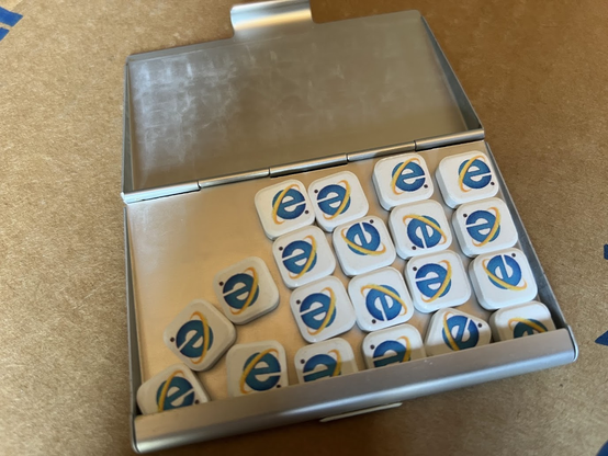Slim silver aluminum case, open, showing several white square thin mints, each printed with the old Internet Explorer lower-case "e" logo with a yellow orbit around it.