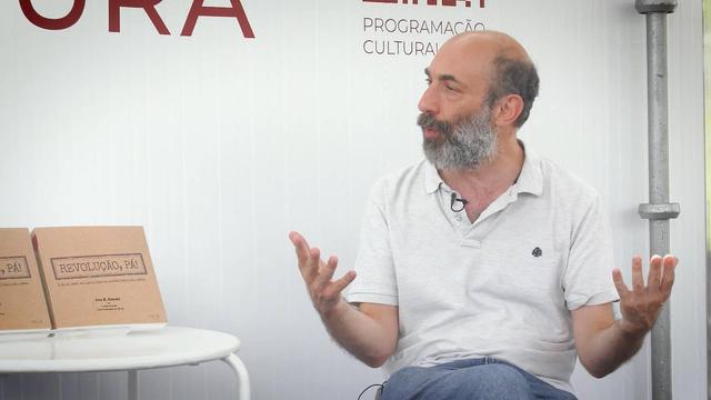 Victor Pereira, sentado no espaço da Santa Casa da Misericórdia de Lisboa na Feira do Livro de Lisboa, a falar junto a uma mesa onde estão expostos os dois volumes do livro "Revolução, Pá!"
