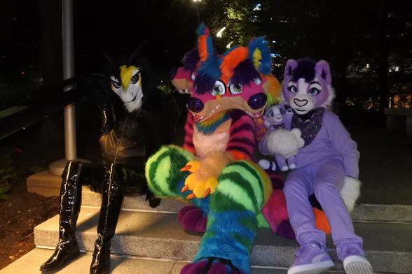 Three fursuiters in Pittsburgh at night, posing on some steps in a small area of park.
On the left is Terry, a white, yellow and black dragon in a leather jacket and PVC jeans.
In the middle is Sherbet, a three-headed Cerberus sparkledog, and on the right is the lavender cat, Heart