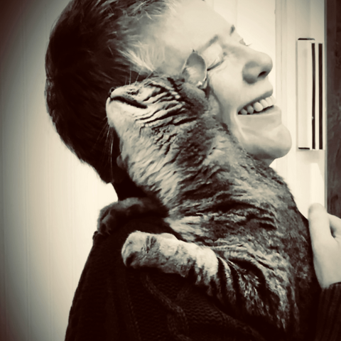 Black and white photo of a short-haired white woman beaming as a tabby cat on her shoulder rubs against her in mutual bliss