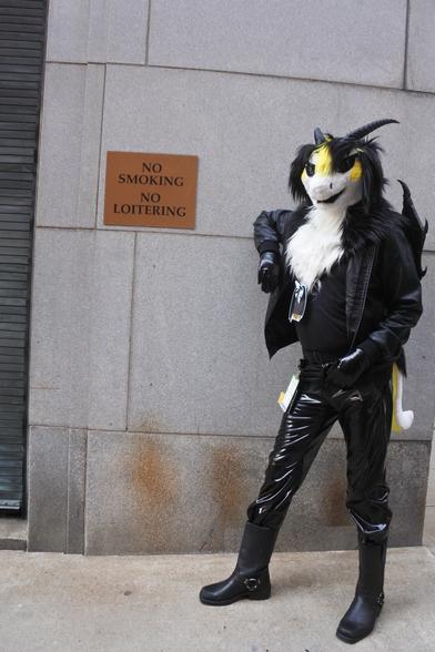 Dragon fursuiter in PVC jeans slouching next to a "no loitering" sign
