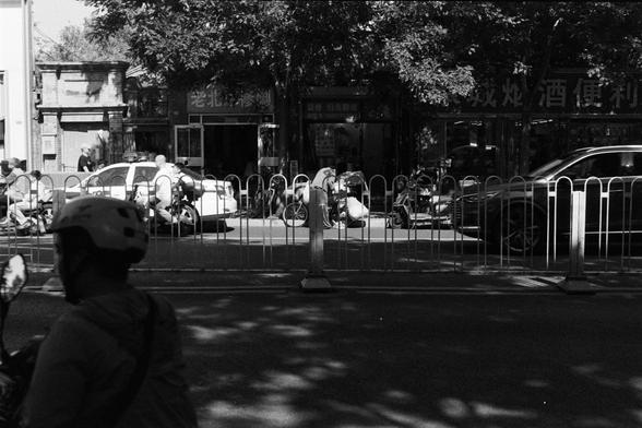 Fujifilm Neopan 100 SS (FF)

**English:**
A black-and-white photograph of a busy urban street scene. In the foreground, a cyclist wearing a helmet is visible. The background shows a variety of people, bicycles, and cars, with a sidewalk barrier separating the street from the sidewalk. The scene is bustling with activity, capturing the essence of a lively city environment.

**Chinese:**
这张黑白照片展示了繁忙的城市街道场景。前景中，一位戴着头盔的骑车人清晰可见。背景中有各种各样的人、自行车和汽车，人行道护栏将街道与人行道分开。这个场景充满活力，捕捉到了充满生机的城市环境的精髓。