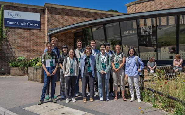 A group of scientists from the Max Planck Institute for Meteorology wearing turquoise name badges and standing in front of the Peter Chalk Centre at the University of Exeter.