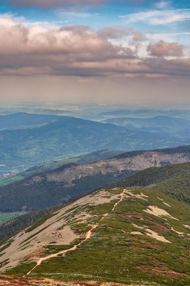 Blick über die Bergketten bei der Schneekoppe im Riesengebirge. Ein weg schlängelt sich durch das Bild. Die karge Tundra Landschaft ist sehr kontrastreich. Rot, Gelb und Grün dominieren. Im Hintergrund wolkenbehangener Himmel  ein wenig blauer Himmel schimmert oben durch