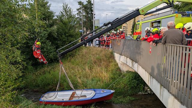 Ein Boot liegt in einem kleinen Bach und ein Feuerwehrmann schwebt darüber