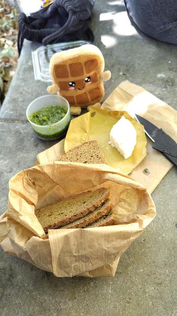 Rafael auf einer Steinkante. Davor ein Glas Pesto, Käse, Brot und ein Messer.