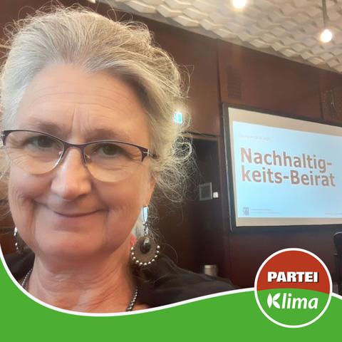 Zu sehen ist ein Selfie unserer Fraktionista Anke, während einer Sitzung des Nachhaltigkeitsbeirats. Sie steht vor einem Durchgang. Auf der rechten Seite ist eine Art Leinwand zu sehen, auf der "Nachhaltig-keits-Beirat" steht.