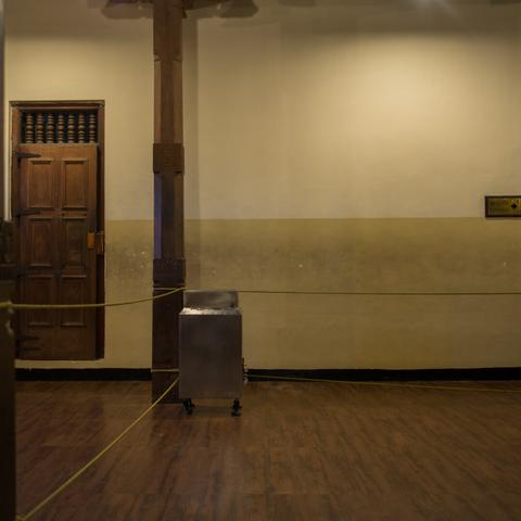 Inside view of a Buddhist temple with a geometric composition.
A door on the left, a box on wheels on its right and rope to prevent people to cross
