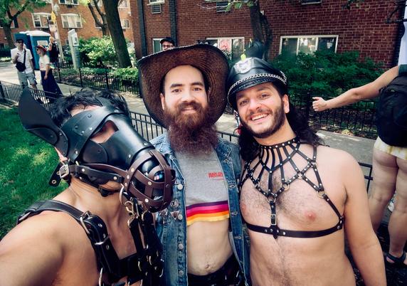A leather pony poses with a man in a crop top, Levi vest, and cowboy hat. Another man stands with an elaborate leather harness and a Muir cap.