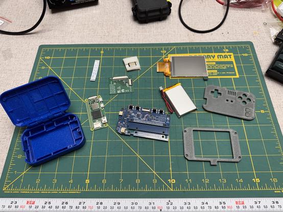 On a workbench sits a cutting mat standing in for a proper esd mat that I don’t own.
On top of the cutting mat sits a handful of 3d printed parts, loose circuit boards, one speaker, a small display, and a LiPo pouch cell battery.