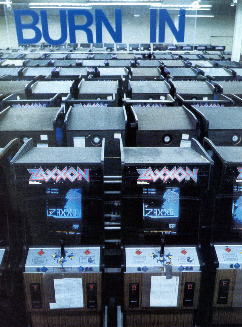 Picture of a giant room of Zaxxon arcade cabinets, each turned on and running the game in attract mode. A sign above the cabinets says "BURN IN" in big letters. This procedure (where the cabinets are left on for a long time) was done as part of the manufacturing process to ensure the cabinets would function reliably once distributed and placed in arcades.