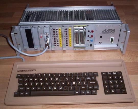 Photo of a silver "MFA" rack-mount computer system, similar in looks to professional lab equipment. On the frontside, S100 modules can be placed into the rack.

A brown and beige keyboard is placed in front of the machine.