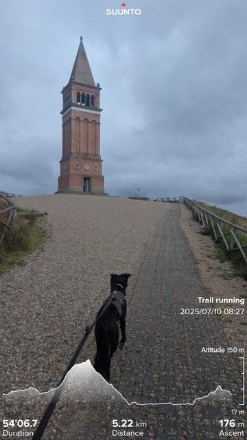 Paddy leading the way up to the top of sky mountain and the red brick tower on a gravel track with grey skies behind. With my running stats imposed on the top