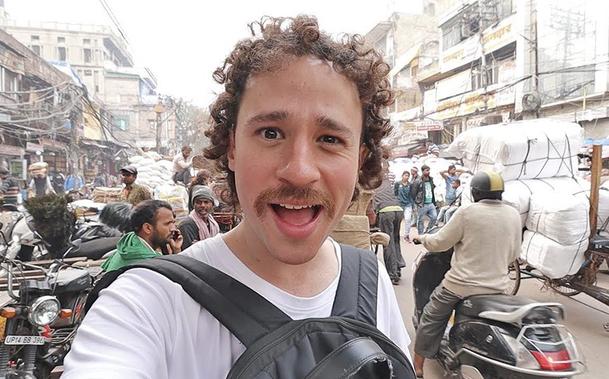 Luisito Comunica, sosteniendo una cámara, en una concurrida calle urbana llena de tráfico y personas.