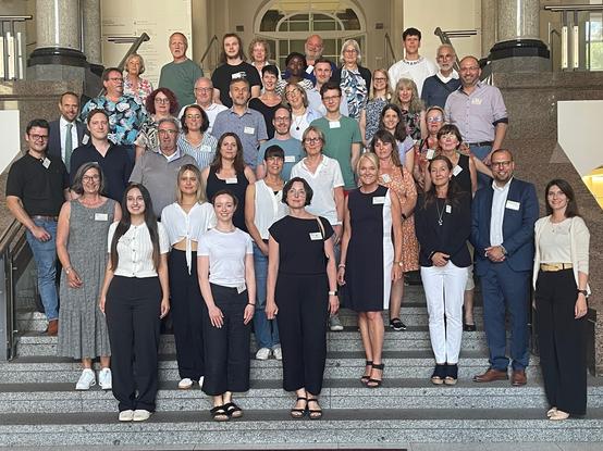 Ein Gruppenfoto mit vielen Erwachsenen auf einer Treppe vor einem Gebäude. Es handelt sich um Teilnehmende des Bürgerforums zum Nichtraucherschutz.