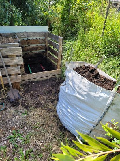 Right compartment of a compost system that is empty with a big bag in front of it filled with compost.