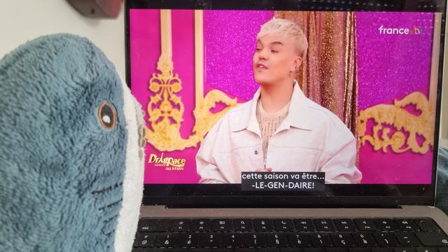 Un blahaj regardant Drag Race France All Star. On voit Nicky Doll dire "cette saison va être Lé-Gen-Daire !"