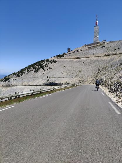 Cyclist descending from Mont Ventoux, the tower at the top visible above the road.