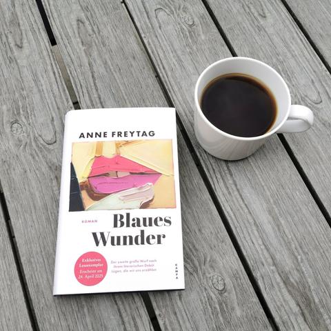 Auf dem Foto ist das Buch Blaues Wunder von Anne Freytag neben einer weißen Tasse auf einem gräulichen Holztisch fotografiert. Im Beitrag geht es um das Buch.