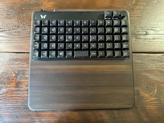 A Keyboard.io Preonic ortholinear 60-key keyboard in a walnut holder.