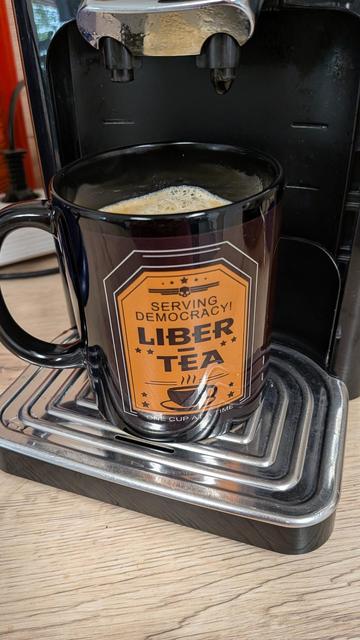 A black mug with an orange sign. "Serving Democracy! LIBER - TEA"
It's a hint to the game Helldivers.