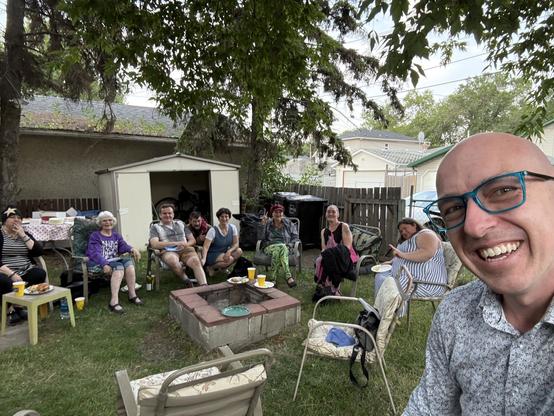 Andrew taking a selfie with a number of other people sitting in lawn chairs outside.