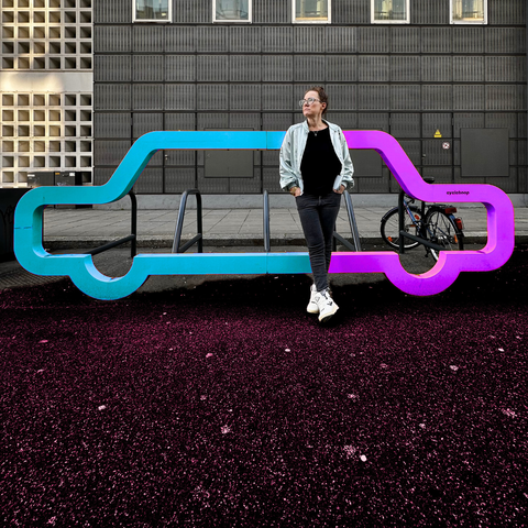 Eine Frau lehnt an einem Radständer, der wie ein Auto gestaltet wurde.