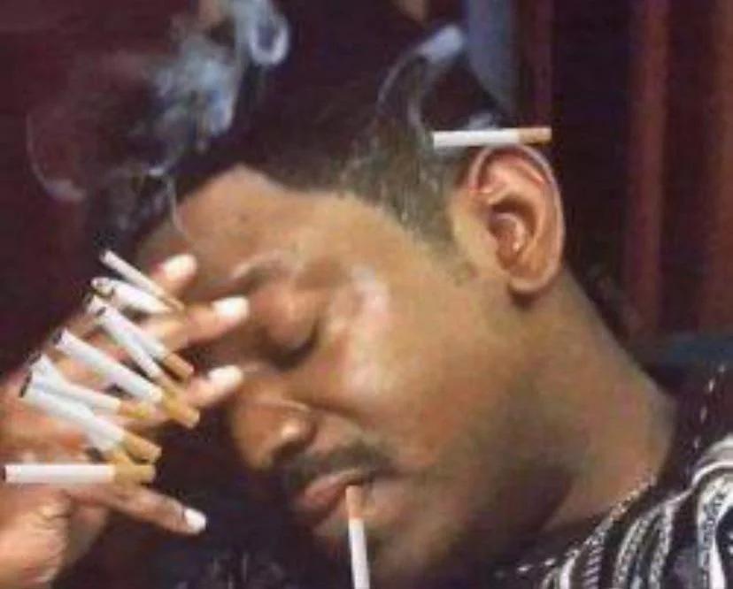 A person is holding 10 cigarettes in one hand, with smoke rising around them. One of the cigarettes is actually a joint.