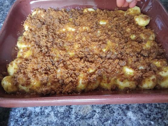 Foto del molde con los cambures ahora parcialmente cubiertos mientras una mano continúa agregando la masa (en forma de migas) que terminará de formar la cubierta...