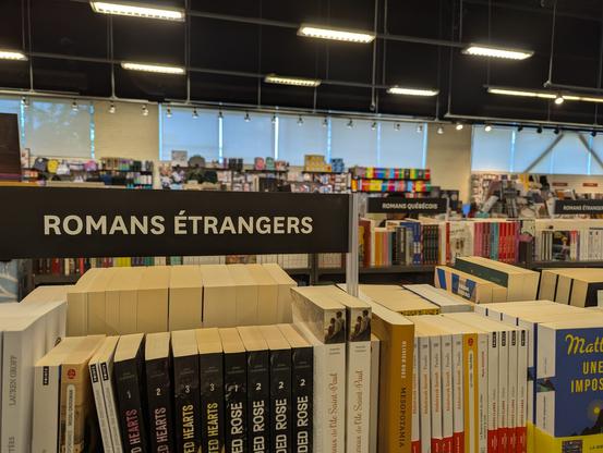 The view across a large bookstore featuring two shelf labels: «Romans étranges» and «Romans québécois»