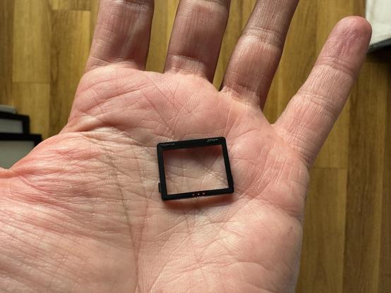 A very small piece of glass in a thin black frame resting in the palm of a man's hands